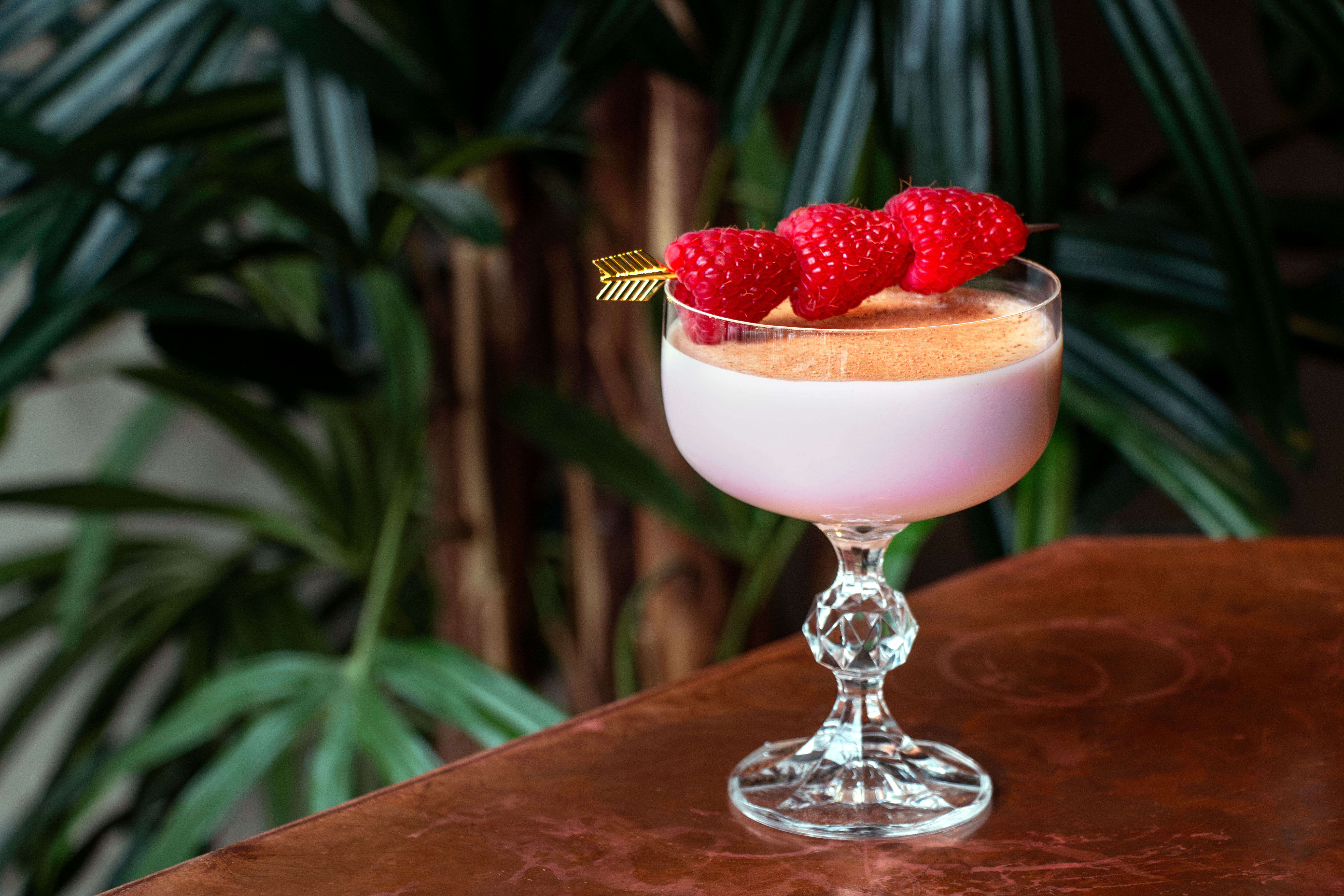 Image of Love at First Flight cocktail topped with raspberries and jungle-like background
