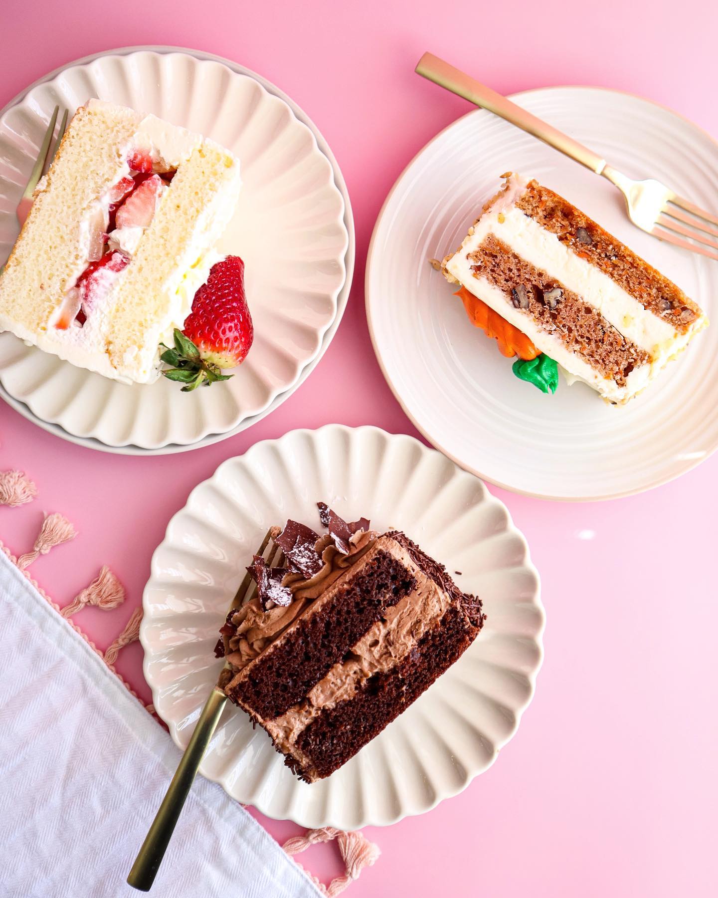 three cake slices on white plates and a pink table. 