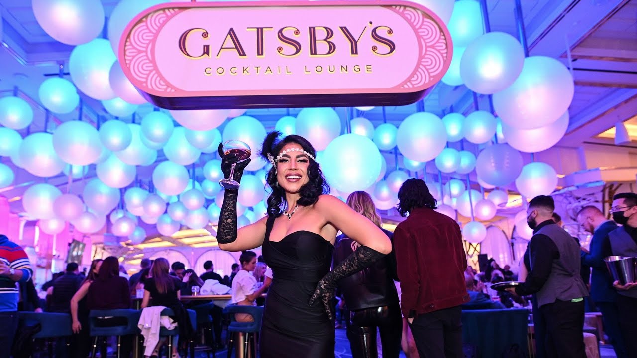 Image of a woman dressed in 1920s attire holding up a drink in front of the Gatsby's Cocktail Lounge sign